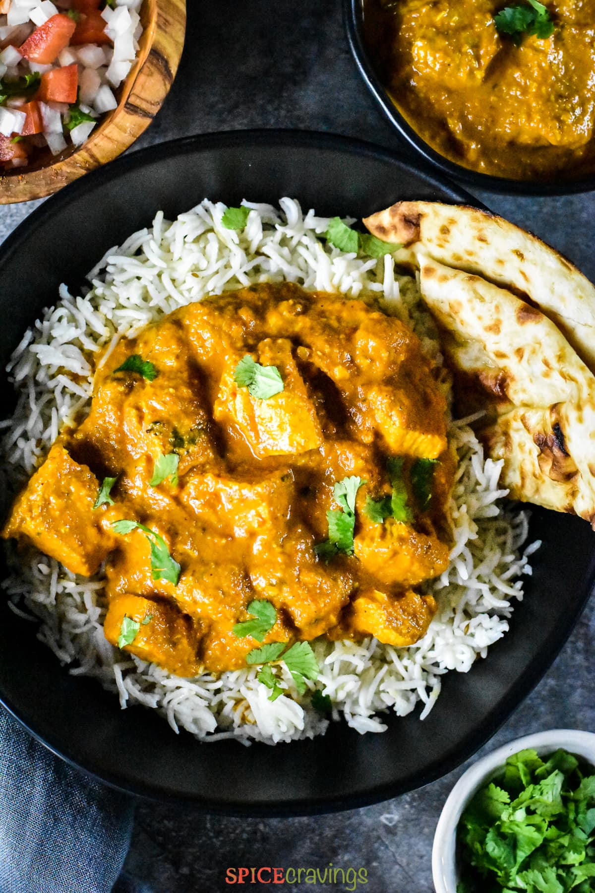 A bowl with chicken tikka masala served ver rice, along with garlic naan