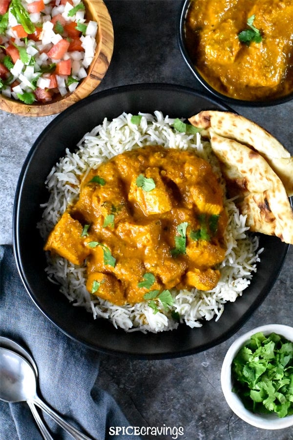 Tender juicy chicken tossed in tikka masala curry, served with rice and naan in a black bowl
