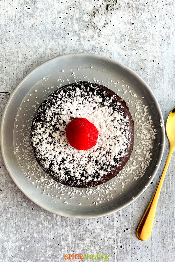 Chocolate cake topped with sugar and a berry on a gray plate