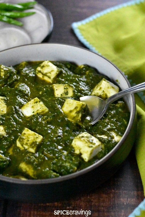 Bowl of paneer cubes in spinach curry, served on a green napkin