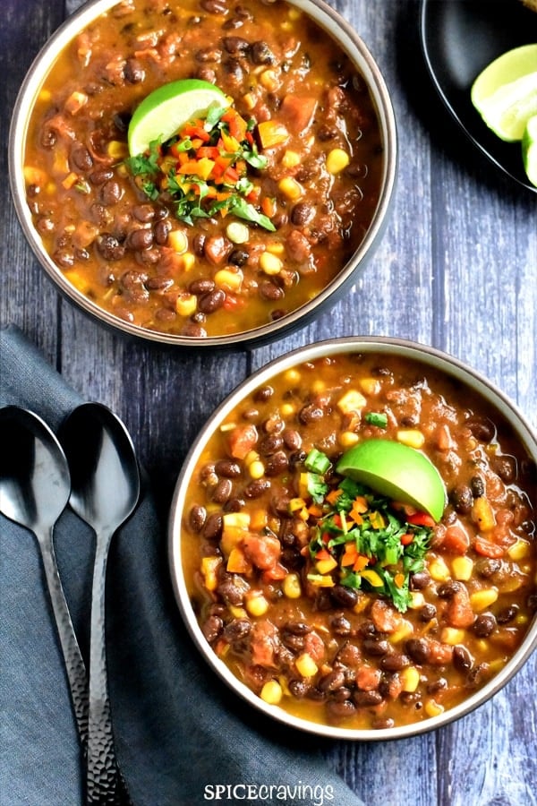 Two bowls on black bean chili topped with peppers, cilantro and lime