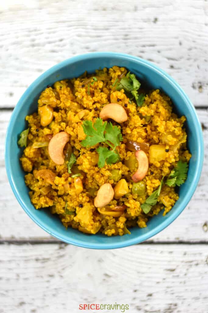 A blue bowl of quinoa Poha garnished with cilantro and cashews