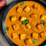 Cubes of paneer in tomato curry garnished with cilantro leaves