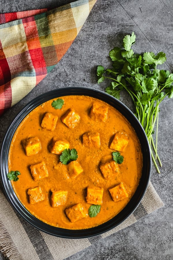 Paneer cubes in tomato gravy with cilantro bunch on side