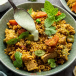 Quinoa and vegetable pilaf in white bowl being topped with mint raita