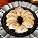Baked Indian Gujiya (sweet dumplings) placed on black plate, dusted with powder sugar