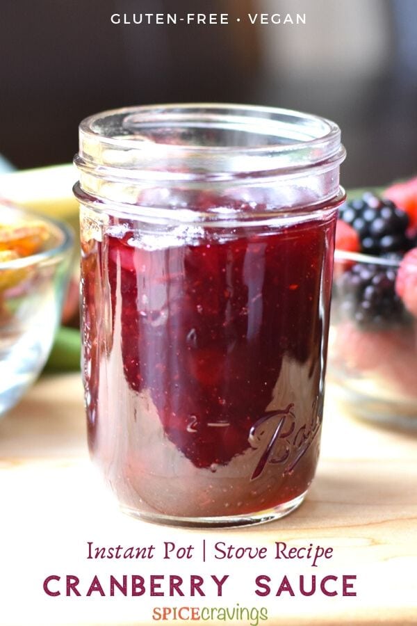 Cranberry sauce stored in a mason jar with berries and crackers on the side