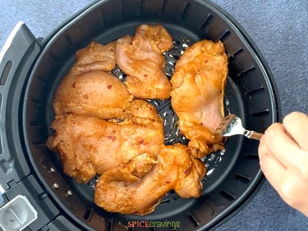 spiced chicken thighs with fork in air fryer