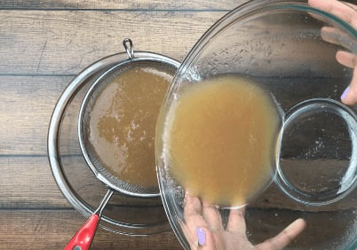 pouring applesauce into fine mesh sieve set over glass bowl