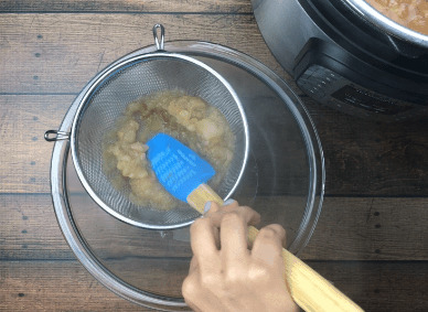 straining apple sauce into bowl with blue spatula