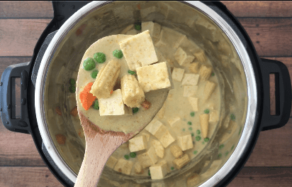 A wooden spoon with thai green curry with vegetables and tofu