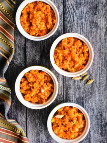 4 ramekins with carrot halwa with green cardamom in the background