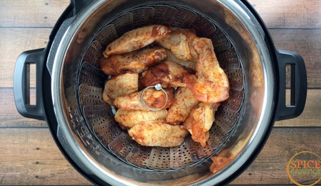 Spiced chicken wings stacked in a steamer basket in Instant Pot