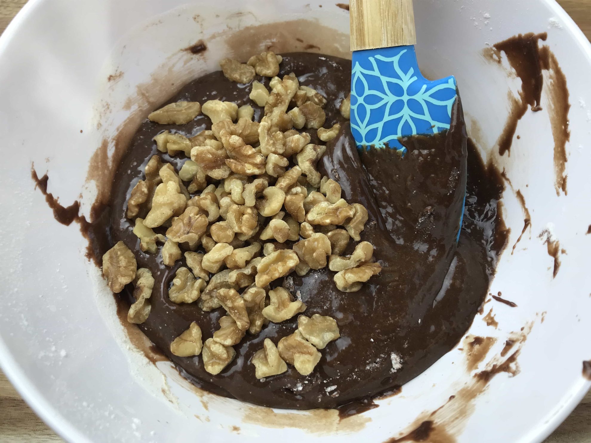 Walnut pieces spread over brownie batter with blue spatula