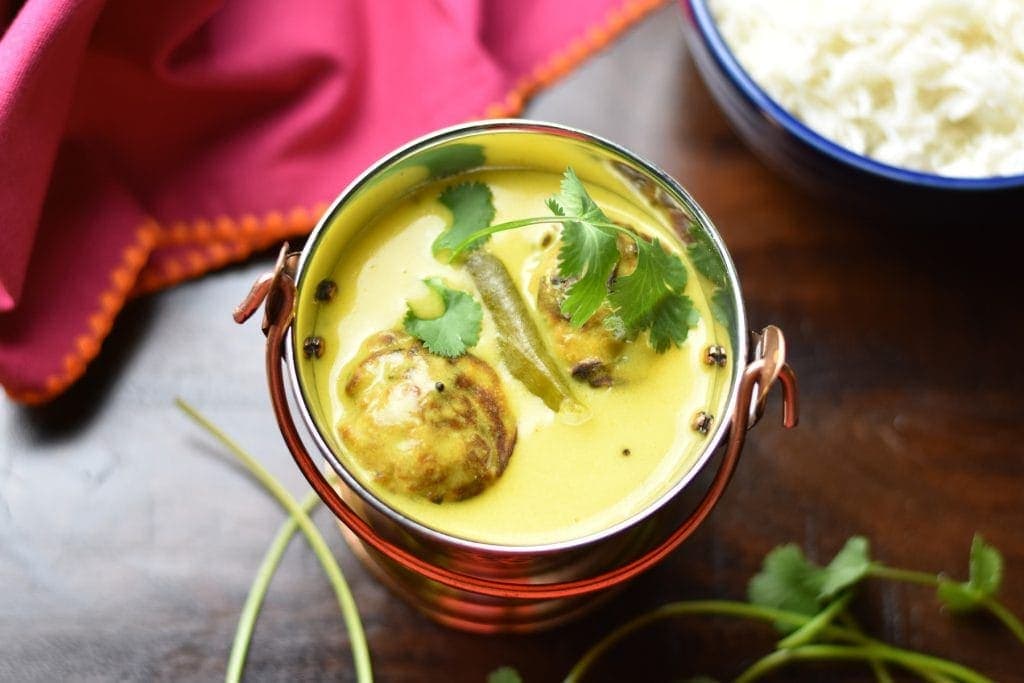 Punjabi kadhi or Yogurt curry with onion-spinach fritters served in a fancy container