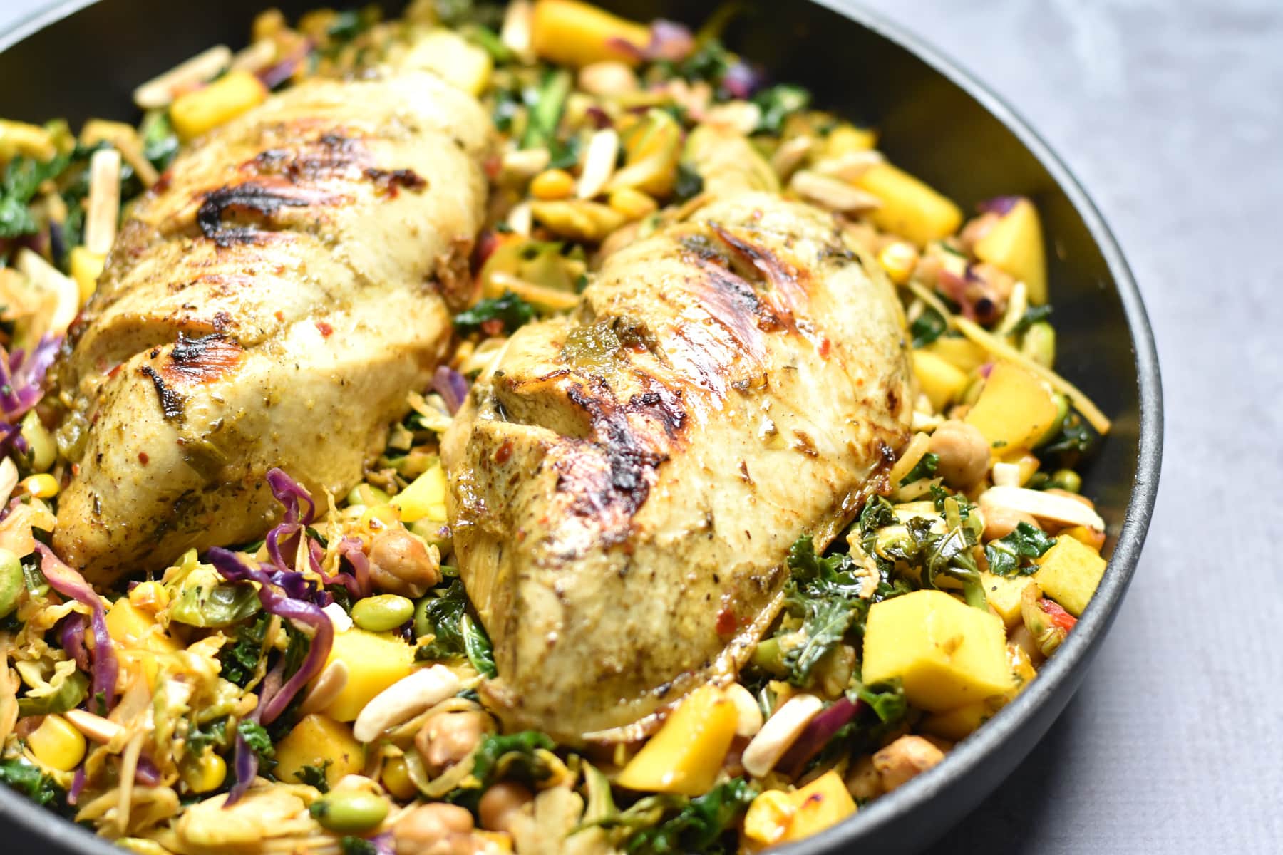 Skillet with grilled chicken breast surrounded by kale and mango salad