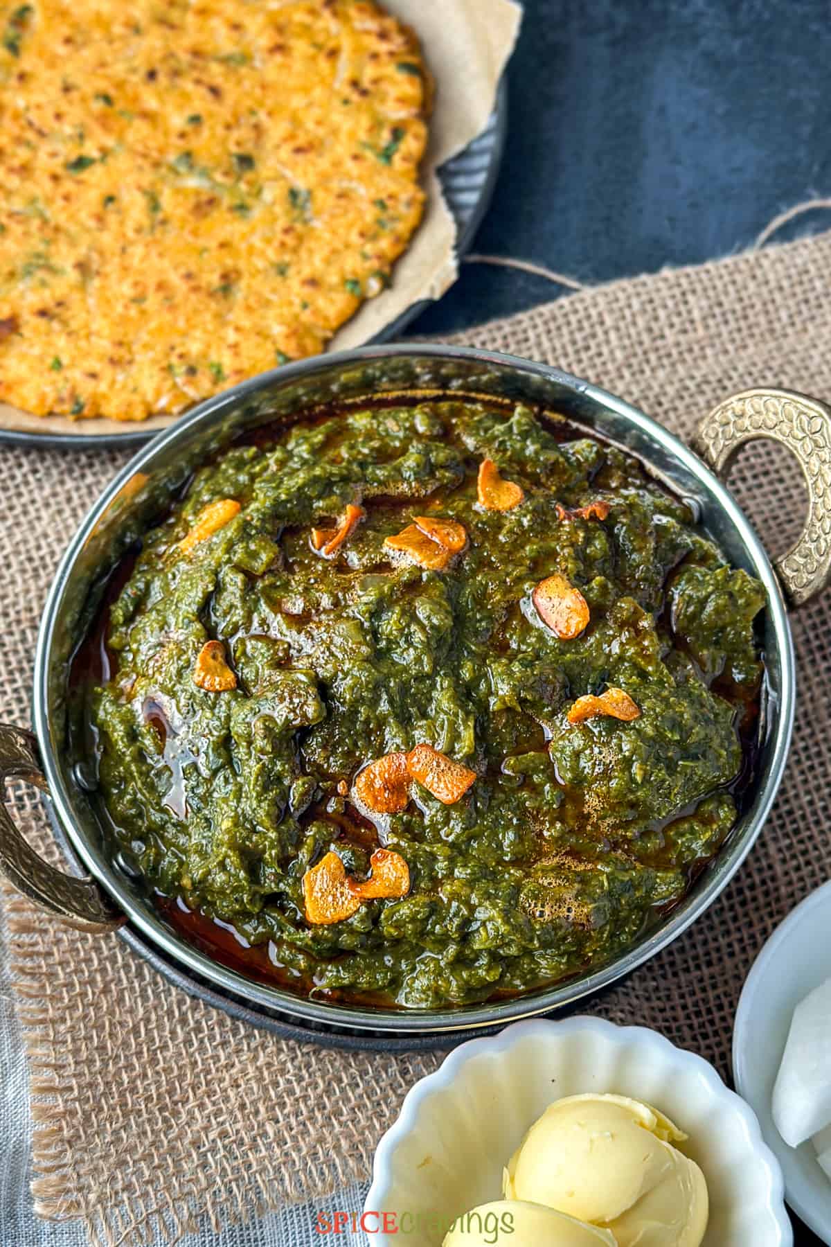 Sarson ka saag (spiced greens) in a copper bowl with garlic and chili oil