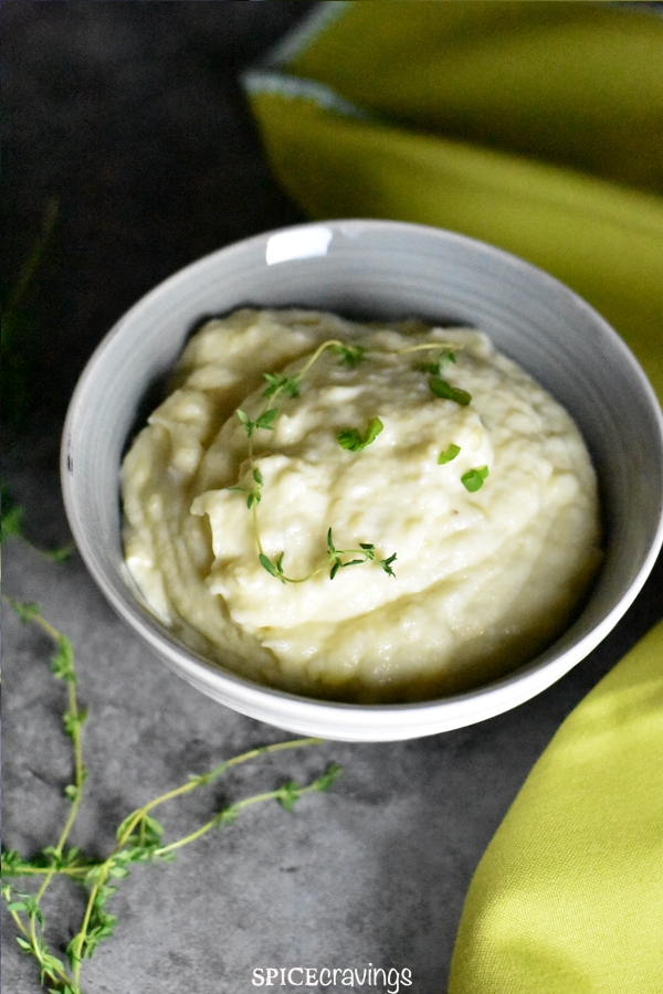 A bowl of garlic mashed potatoes garnished with thyme leaves