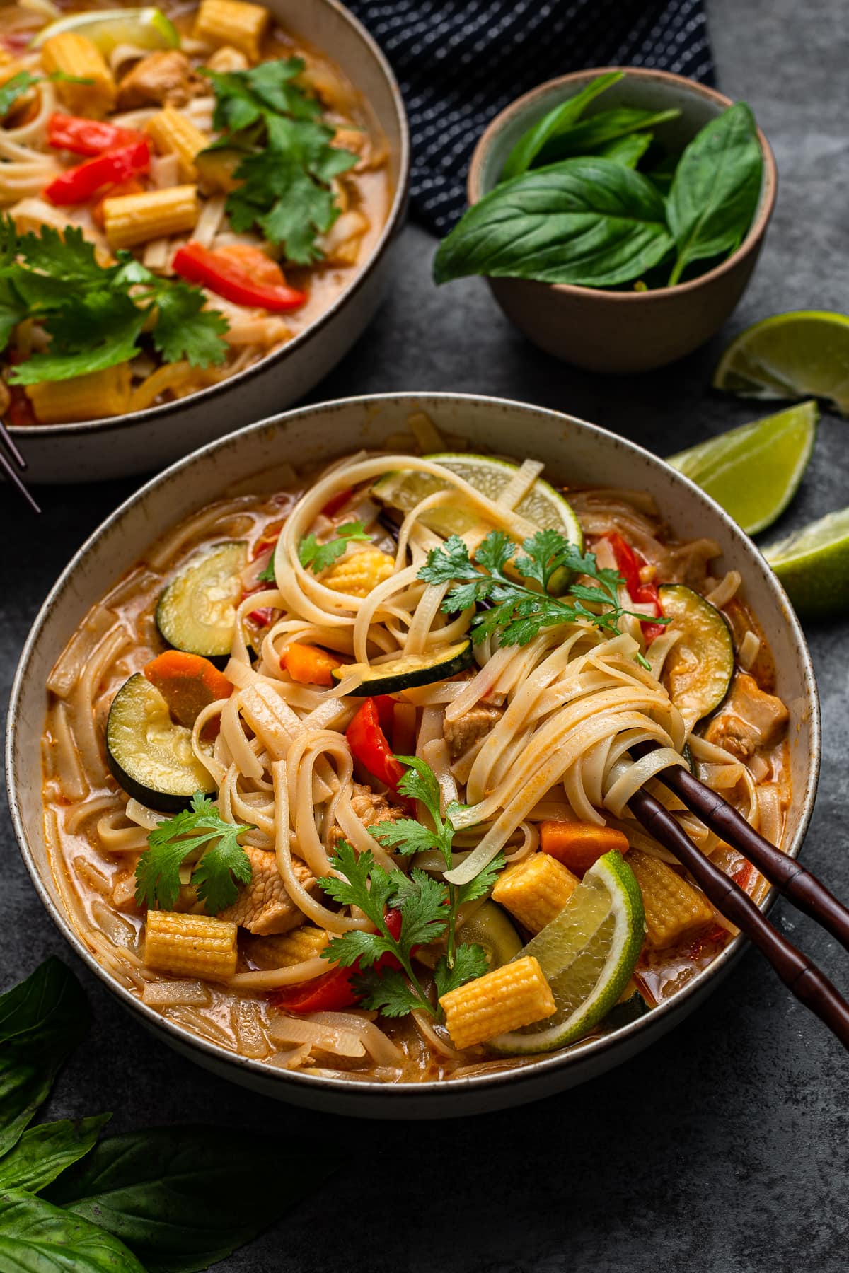 Curry soup bowl with vegetables, chicken, lime and noodles wrapped in chopsticks