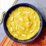 Badam halwa served in a blue bowl with slivered almonds on top