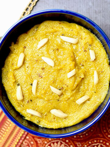 Badam halwa served in a blue bowl with slivered almonds on top