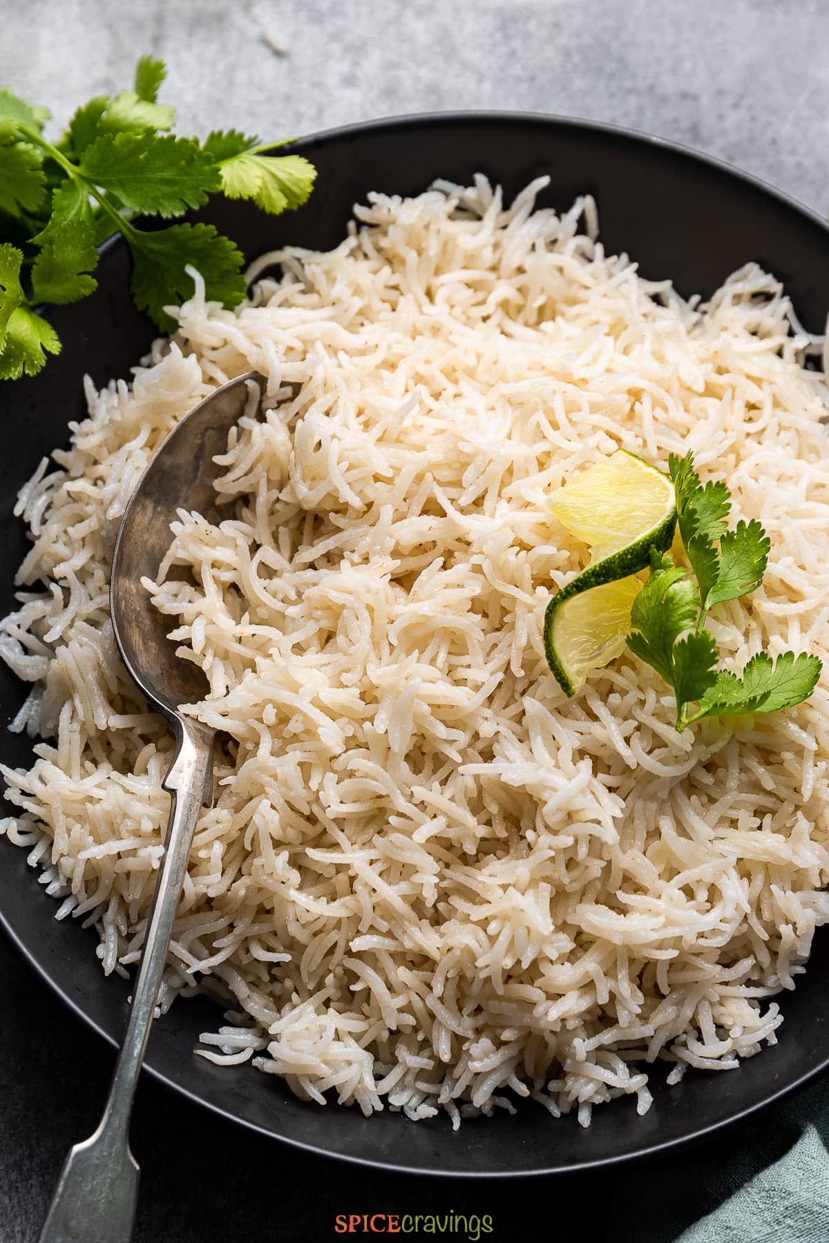 coconut rice in black bowl with spoon garnished with cilantro and lime wedge