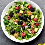 berry arugula salad tossed with strawberry vinaigrette in white bowl with serving spoons