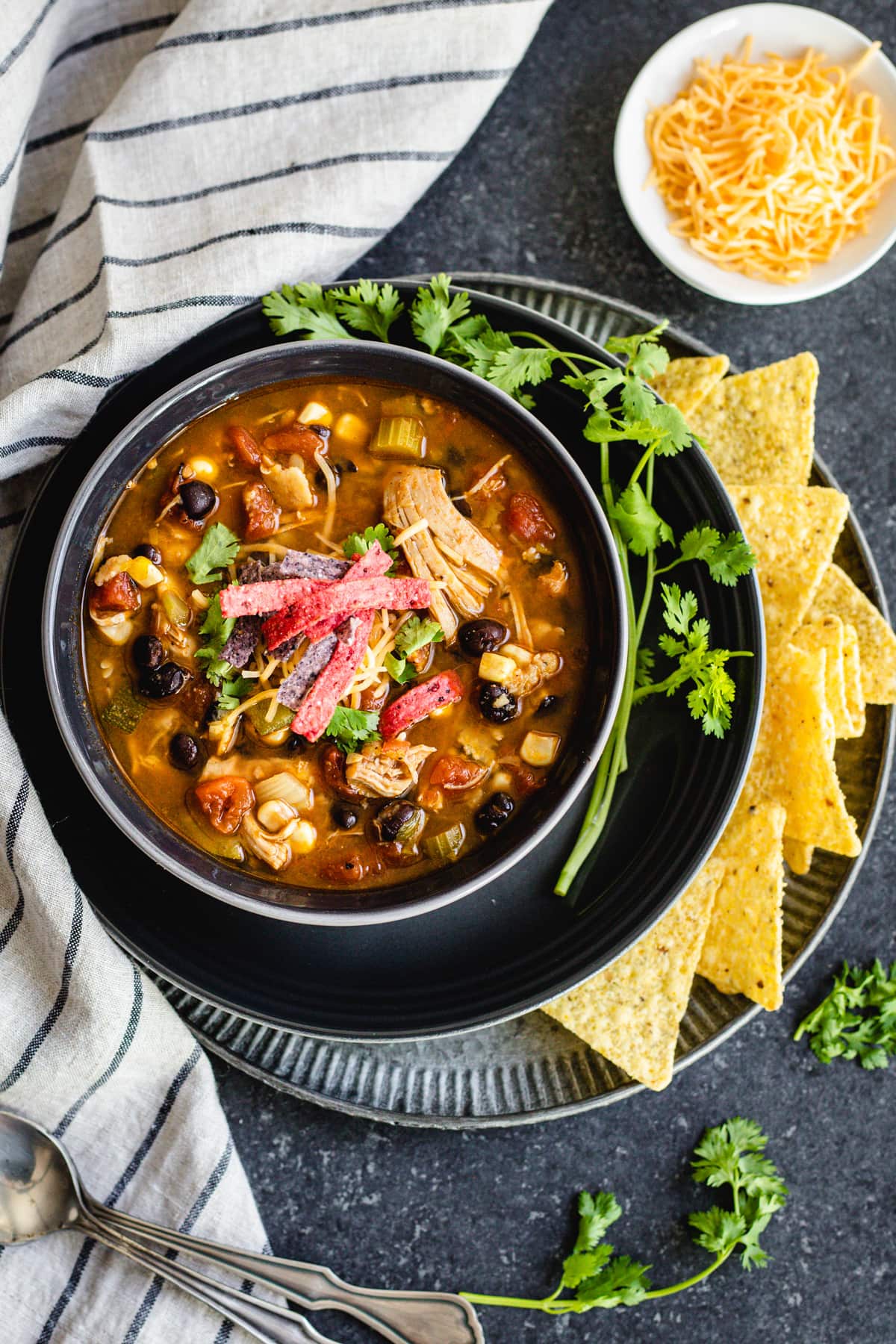 chicken tortilla soup in black bowl with cilantro sprigs and tortilla chips