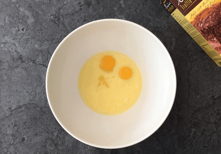 Adding eggs to the melted butter in a bowl.