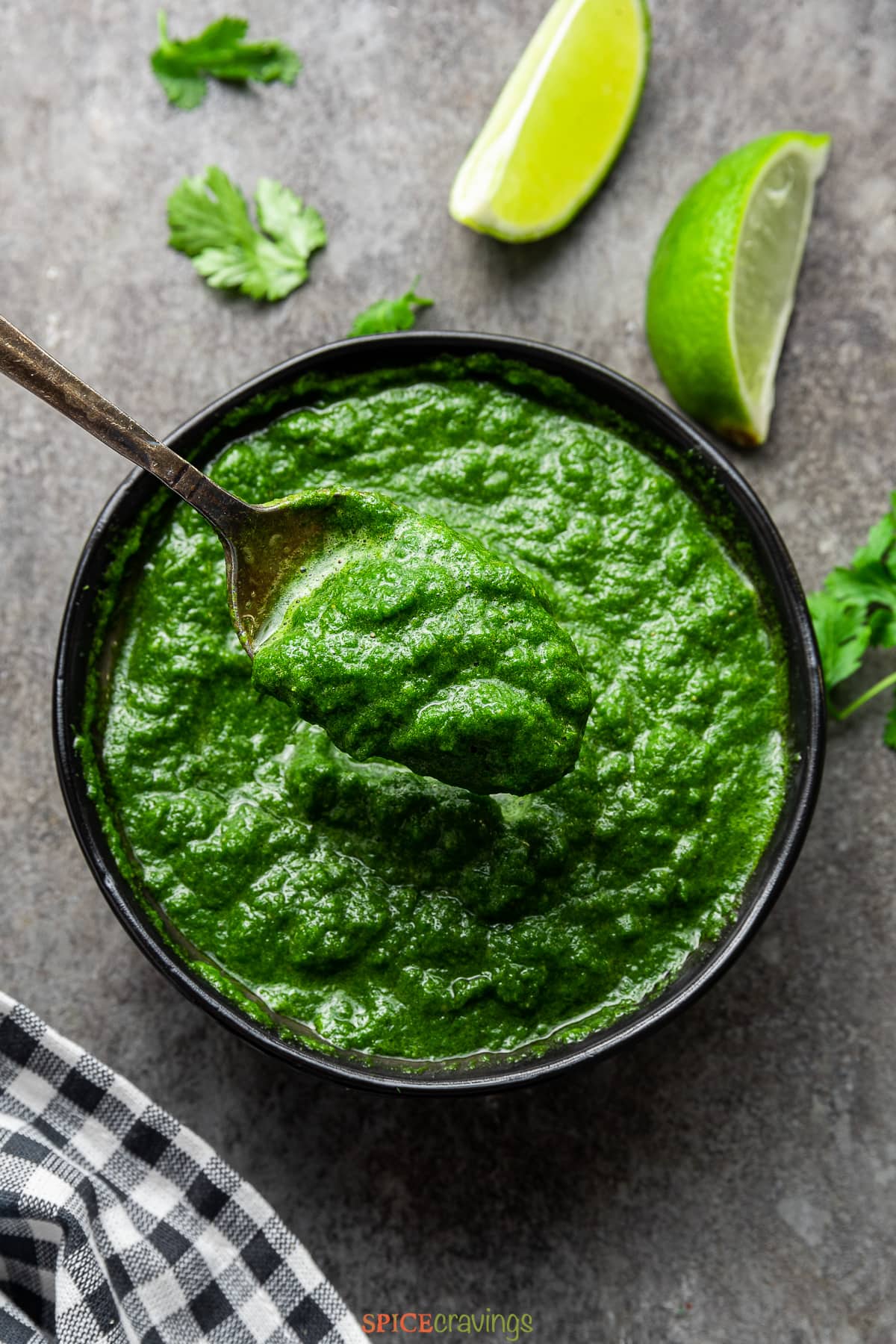 Lifting a spoon full of Indian green chutney from a black bowl