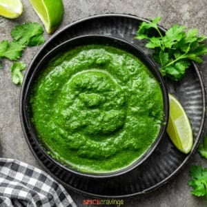 Indian Green chutney in a black bowl next to cilantro and lime
