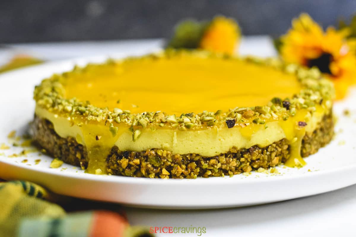 Side view of mango topping dripping on the sides of a mango pistachio cheesecake
