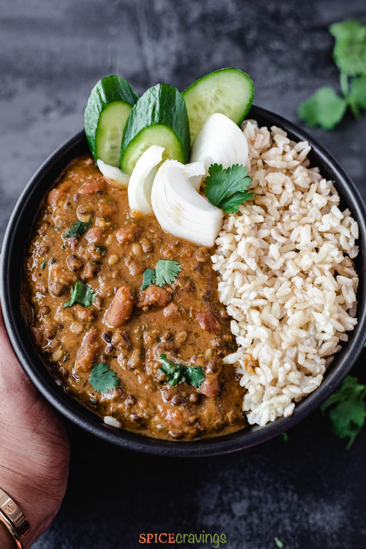 A bowl made with Dal Makhani, brown rice, sliced onions and cucumbers