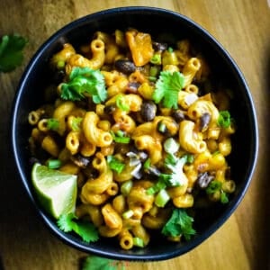 Black bowl with cheesy pasta and beans, garnished with cilantro
