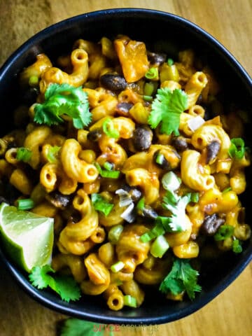 Black bowl with cheesy pasta and beans, garnished with cilantro