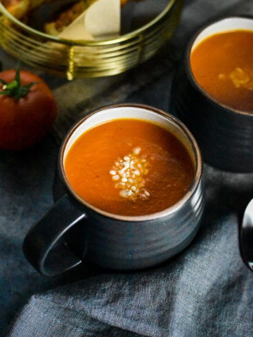 A cup of Roasted Red Pepper Tomato Soup garnished with parmesan cheese