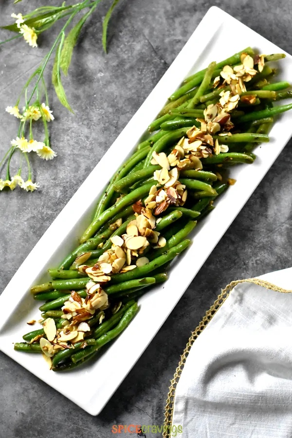 A white plate with crisp green string beans topped with almonds