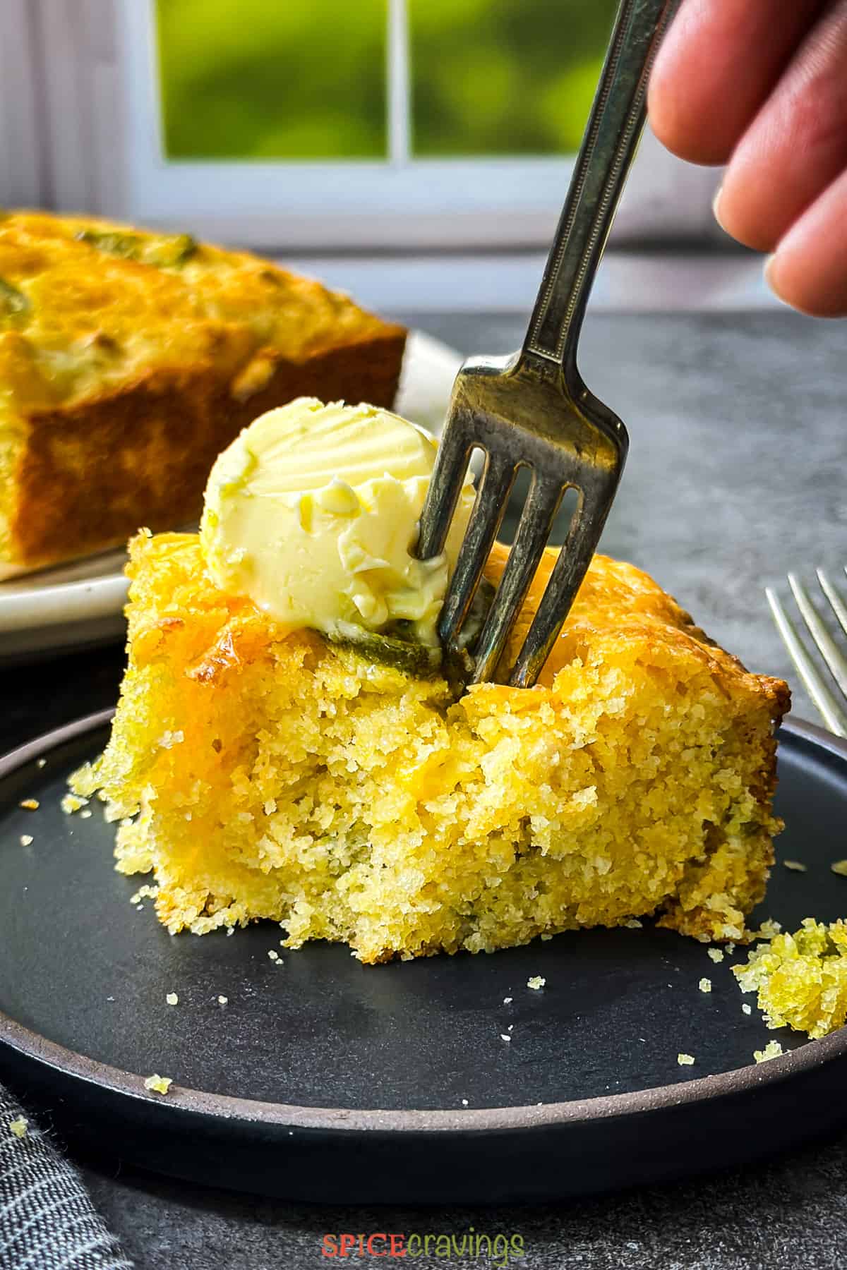 A fork cutting through butter into a slice of cornbread