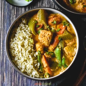 Red curry served with brown rice in a brown bowl on a wooden backdrop