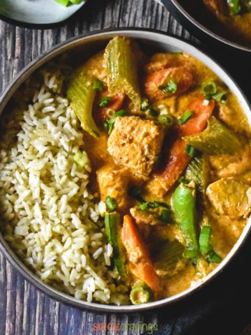 Thai red curry served with brown rice in a brown bowl on a wooden backdrop