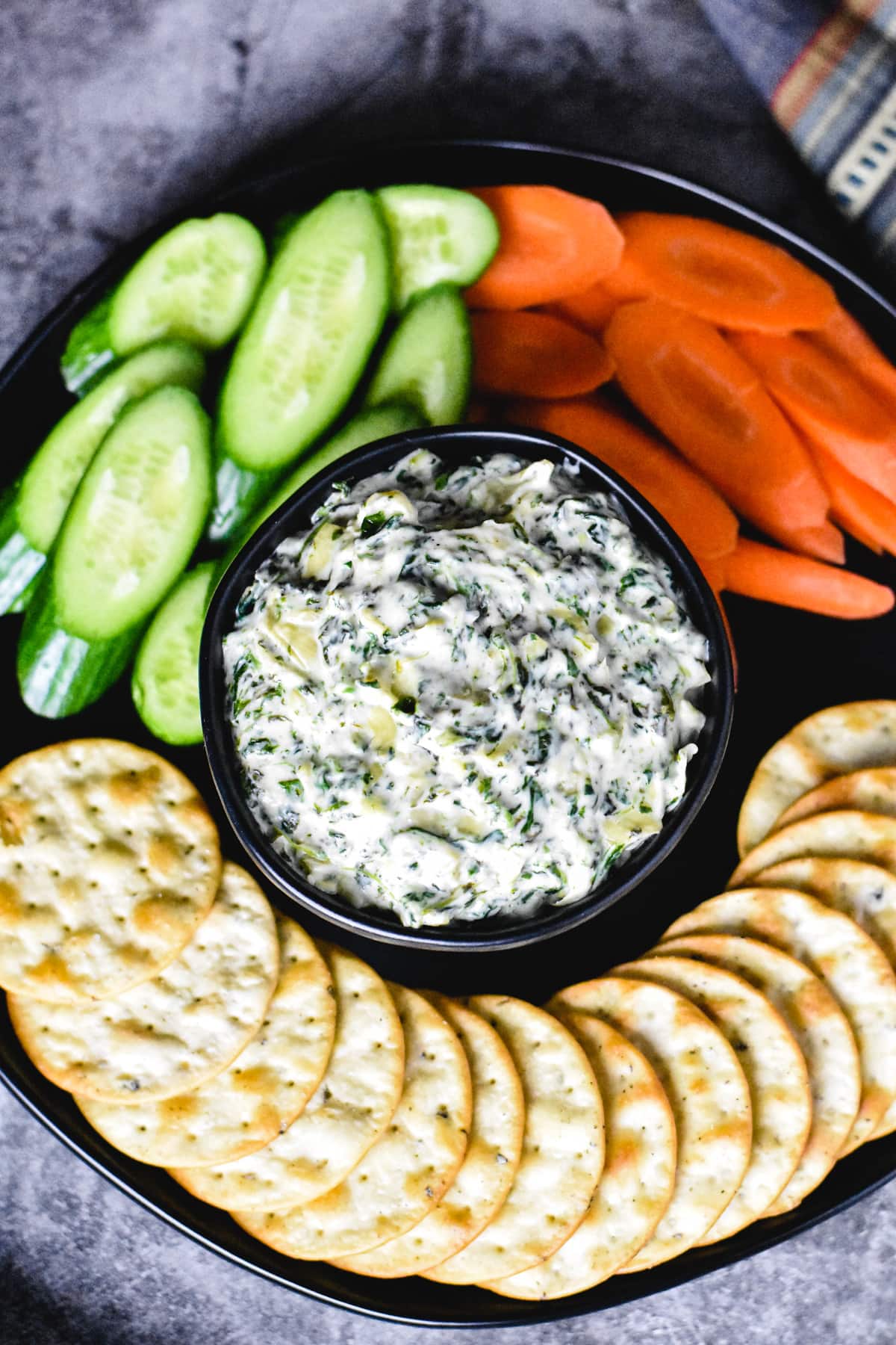Spinach artichoke dip in bowl with carrots, cucumber and crackers