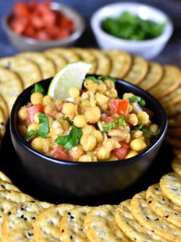 A bowl of white peas dip garnished with onions, tomato, cilantro and a wedge of lime