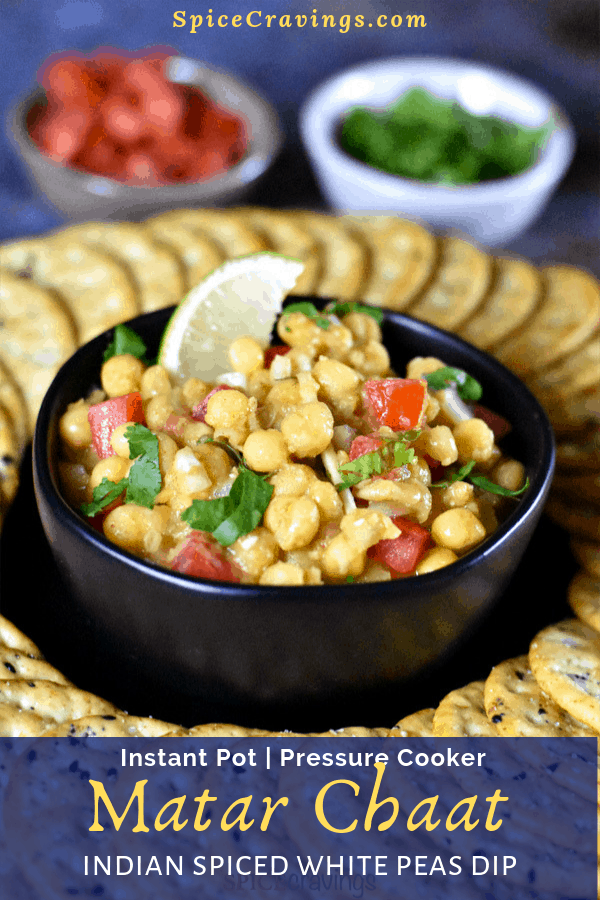 A bowl of white peas dip garnished with onions, tomato, cilantro and a wedge of lime