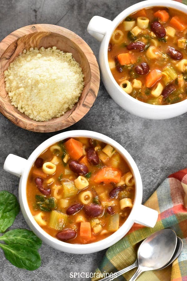 Two white bowls with pasta fagioli soup served with a bowl of grated parmesan cheese