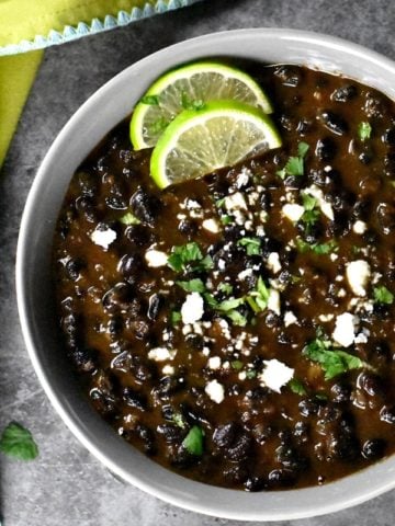 A bowl of creamy black beans garnished with lime slices and cotija cheese