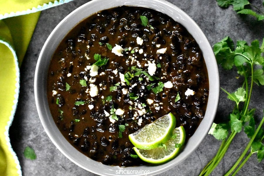 A bowl of black beans with sprigs of cilantro on the right hand side