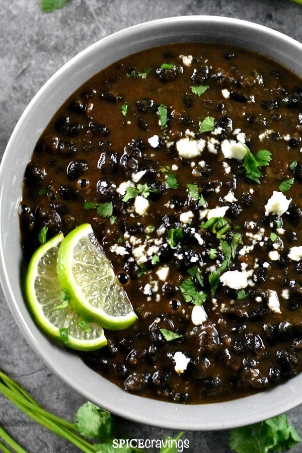 A grey bowl of creamy black beans made in tex-mex style, garnished with cilantro and lime