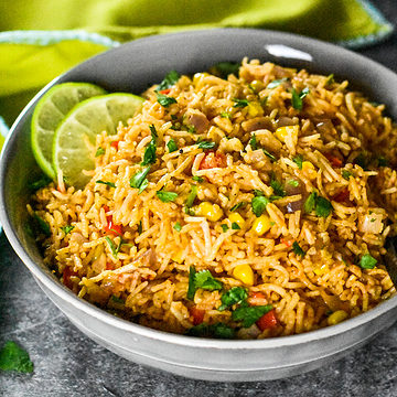 Mexican rice with corn and cilantro served in a grey bowl with a lime green napkin