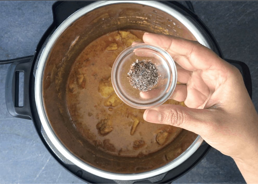 Adding cardamom powder to the chicken curry