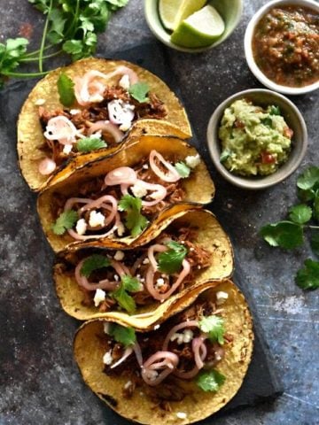 Four corn tortillas filled with crispy carnitas, garnished with onions and cilantro